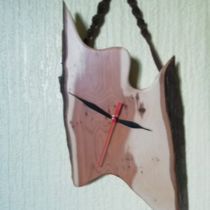 May include: A wooden clock with a unique, irregular shape, hanging from a brown rope. The clock face has a red hour hand and a black minute hand.