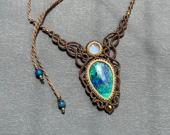 Könnte beinhalten: Eine braune Makramee-Halskette mit einem großen grünen und blauen Edelstein-Anhänger und einem kleineren weißen Edelstein. Die Halskette hat zwei braune Schnüre mit blauen Perlen an den Enden.