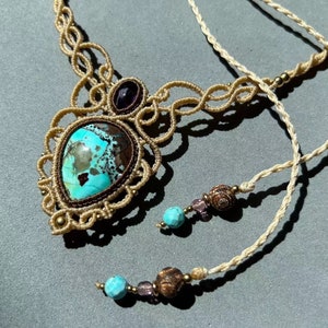 May include: A turquoise and brown gemstone pendant necklace with a macrame design. The necklace is made with beige cord and features small turquoise and brown beads.