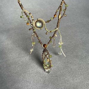 May include: A white and brown macrame necklace with a clear quartz crystal pendant and green and brown beads. The necklace has a moonstone cabochon in the center.