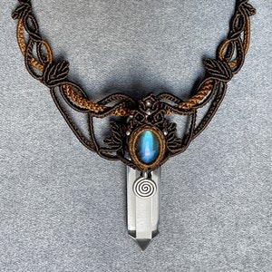 May include: A brown and gold macrame necklace with a blue labradorite stone and a clear quartz crystal pendant. The pendant has a silver spiral charm.