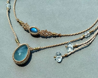 May include: A double-strand necklace with a blue aquamarine pendant and a smaller oval labradorite pendant. The necklace is made with macrame cord and gold beads.