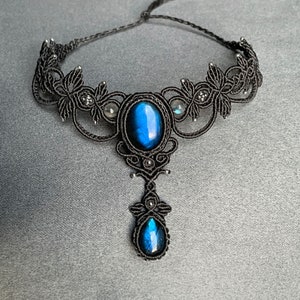 May include: A black macrame choker necklace with a large blue labradorite gemstone pendant. The necklace features intricate knotwork and smaller labradorite stones.
