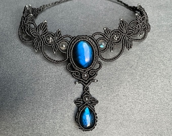 May include: A black macrame choker necklace with a large blue labradorite gemstone pendant. The necklace features intricate knotwork and smaller labradorite stones.
