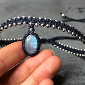 May include: A black and silver bracelet with a moonstone pendant. The bracelet is made of cord and silver beads.