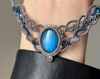May include: A silver and blue macrame choker necklace with a large oval labradorite gemstone pendant.