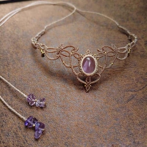 May include: A handmade macramé necklace with a central oval, pale purple gemstone. The necklace has intricate knotwork in a light brown colour, with small gold beads. Two matching beaded strands with purple amethyst stones are also included.