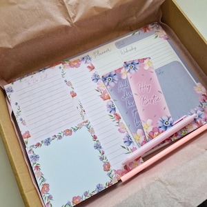May include: A set of floral patterned stationery with a pink pen. The stationery includes a to-do list, a planner, a notes section, and a note pad. The note pad has the text "Hey bestie be..." on it.