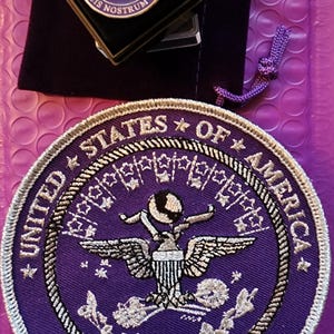 May include: Purple embroidered patch with the words "United States of America" and "Military Brats" in white. The patch features a silver eagle with wings spread and a globe in its talons.