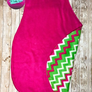 May include: A pink fleece baby blanket with a green and white chevron pattern on the reverse side.  The blanket is shaped like a large oval.
