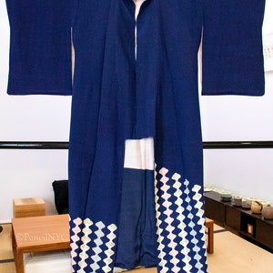 May include: A dark blue Japanese kimono with a white and light blue geometric pattern on the bottom hem. The kimono is hanging on a rack.