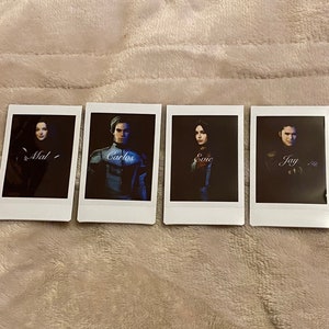 May include: Four white Polaroid-style photos with images of people. Each photo has a name written on it: Mal, Carlos, Evie, and Jay. The photos are arranged in a row on a light brown, textured surface.