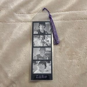 Peut inclure: Marque-page noir et blanc avec quatre images d'une personne. Le marque-page a un pompon violet et le nom "Luke" en bas. Les images semblent provenir d'une séance photo.