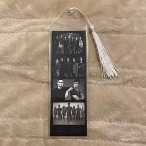 May include: A clear plastic bookmark featuring black and white images of the cast of Teen Wolf. The bookmark has a white tassel attached at the top. The words "Teen Wolf" are printed at the bottom.