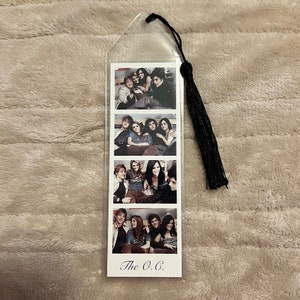 Könnte beinhalten: Transparenter Kunststoff-Lesezeichen mit vier Fotostreifen, die eine Gruppe von Personen zeigen. Eine schwarze Quaste hängt oben. Der Text "The O.C." ist unten auf dem Lesezeichen aufgedruckt.