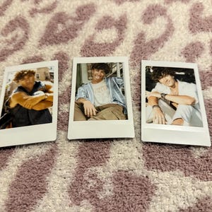 May include: Three instant photo prints featuring a young person in various poses. The photos are in white frames and show the person in different outfits and settings. The background is a patterned, textured surface.