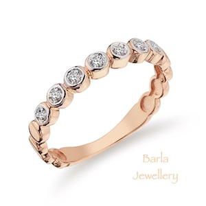 Puede incluir: Un anillo de banda de oro rosa con una fila de pequeños diamantes redondos engastados en la banda. El anillo es un diseño delicado y simple.