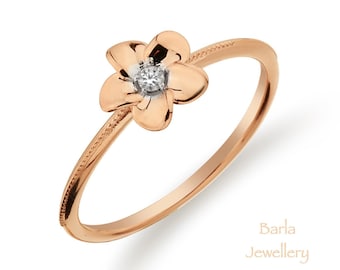 Può includere: Un anello in oro rosa con un delicato design a fiore e un piccolo diamante al centro. L'anello è su uno sfondo bianco.