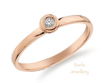 May include: A simple rose gold band ring with a single round diamond set in a bezel setting.