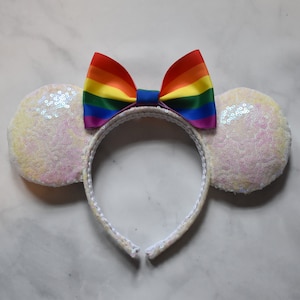May include: White sequined Minnie Mouse ears with a rainbow ribbon bow.