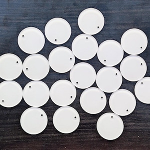 May include: A collection of twenty-one white, circular objects with a small black hole near the edge of each. The objects are arranged on a dark wood-grain surface.