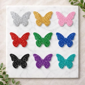 May include: A set of nine butterfly-shaped cutouts arranged in a three-by-three grid. Each butterfly features a distinct glittery finish in silver, gold, pink, red, green, blue, black, purple, and teal, displayed on a white marble surface.