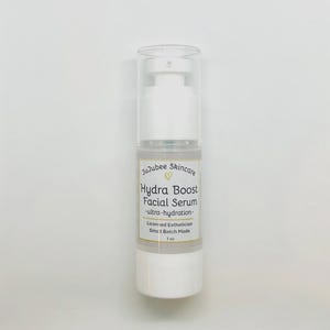 Pu&ograve; includere: Una bottiglia bianca di siero viso Hydra Boost di JuJubee Skincare. L'etichetta include il testo "ultra-hydration", "Licensed Esthetician" e "Small Batch Made". La bottiglia &egrave; da 29,5 ml.