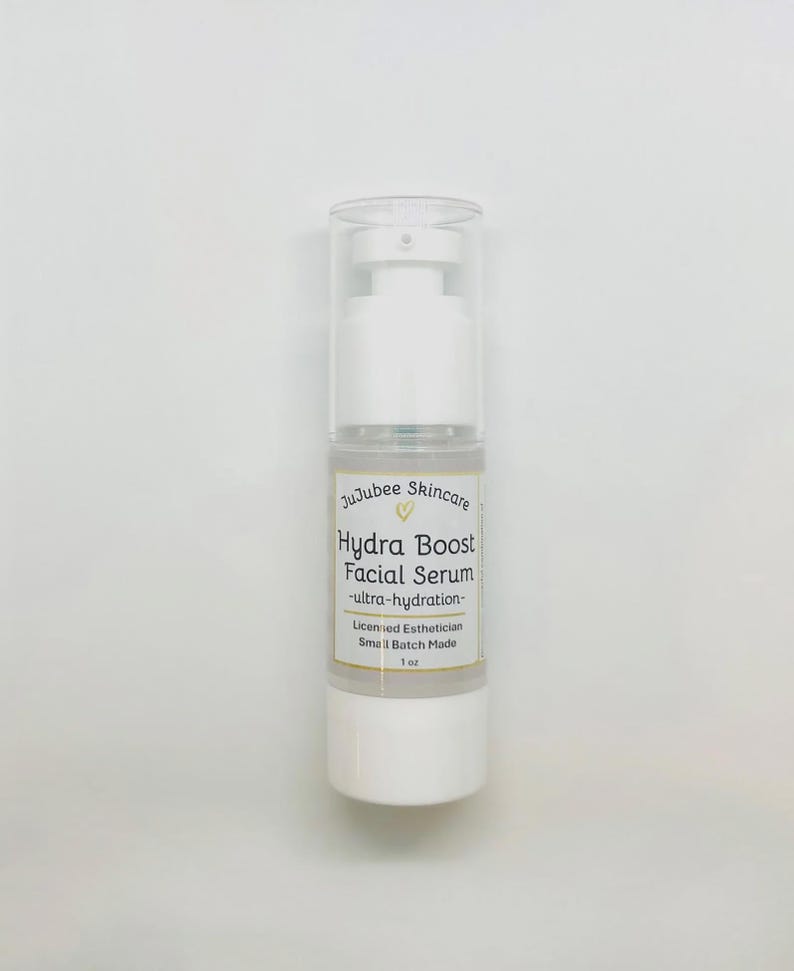Pu&ograve; includere: Una bottiglia bianca di siero viso Hydra Boost di JuJubee Skincare. L'etichetta include il testo "ultra-hydration", "Licensed Esthetician" e "Small Batch Made". La bottiglia &egrave; da 29,5 ml.