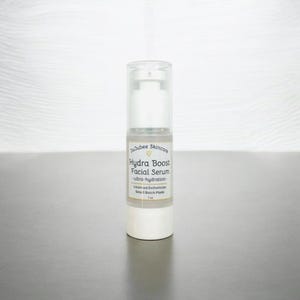 Pu&ograve; includere: Flacone di siero viso bianco e trasparente con dosatore a pompa. L'etichetta recita "JuJubee Skincare Hydra Boost Facial Serum - ultra-hydration". Il flacone &egrave; da 30 ml. Il prodotto &egrave; su una superficie grigia.
