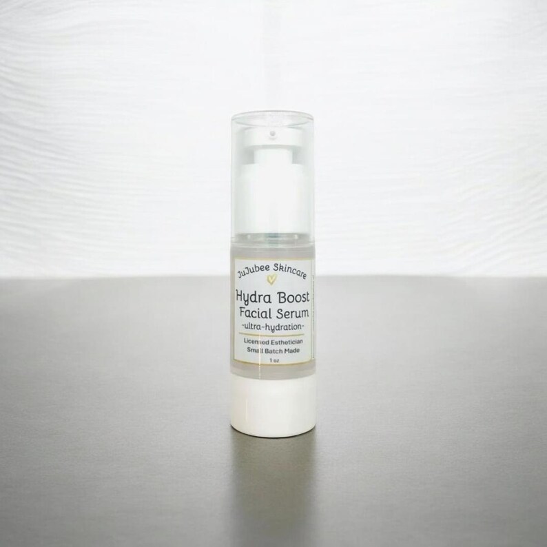 Pu&ograve; includere: Flacone di siero viso bianco e trasparente con dosatore a pompa. L'etichetta recita "JuJubee Skincare Hydra Boost Facial Serum - ultra-hydration". Il flacone &egrave; da 30 ml. Il prodotto &egrave; su una superficie grigia.