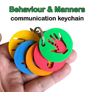 May include: A communication keychain with the text "Behaviour & Manners". The keychain features several round, brightly coloured discs in yellow, blue, orange, red, and green. Each disc has a unique cutout design, held together by a metal ring.