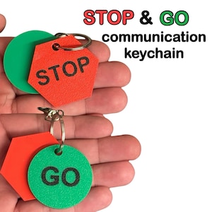 May include: A communication keychain with red and green tags. One tag is a red hexagon with the word "STOP" in black. The other tag is a green circle with the word "GO" in black. The text "STOP & GO communication keychain" is in the background.