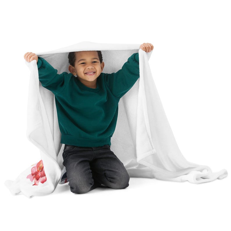 May include: A young person wearing a green sweater and black pants is sitting under a white blanket. The blanket has a pink floral design on one corner.