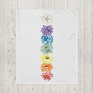 May include: A white throw blanket with a vertical row of seven watercolor flowers in rainbow colors. The flowers are arranged from top to bottom in the following order: white, purple, blue, green, yellow, orange, and red.