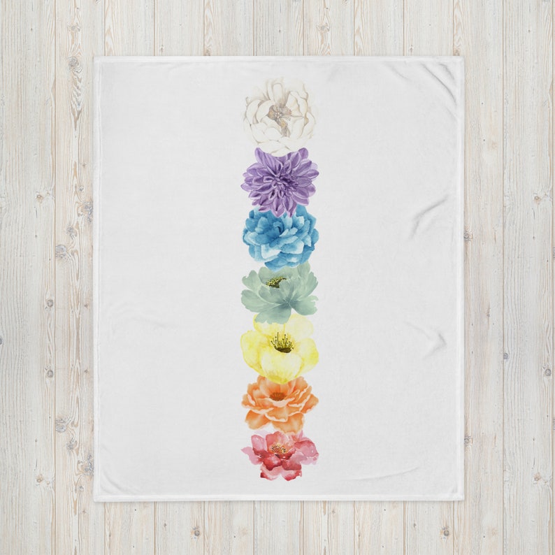 May include: A white throw blanket with a vertical row of seven watercolor flowers in rainbow colors. The flowers are arranged from top to bottom in the following order: white, purple, blue, green, yellow, orange, and red.