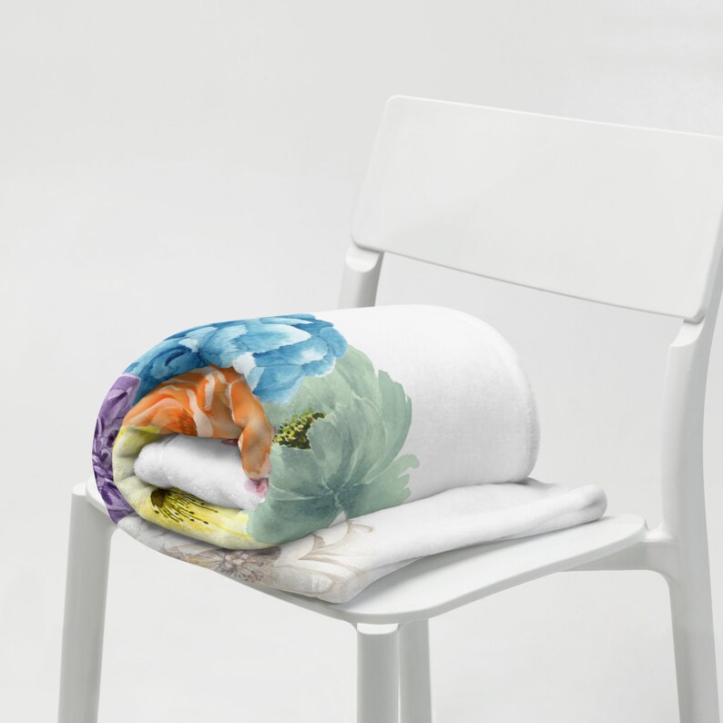 May include: A white fleece blanket with a colorful floral print. The blanket is rolled up and placed on a white chair.