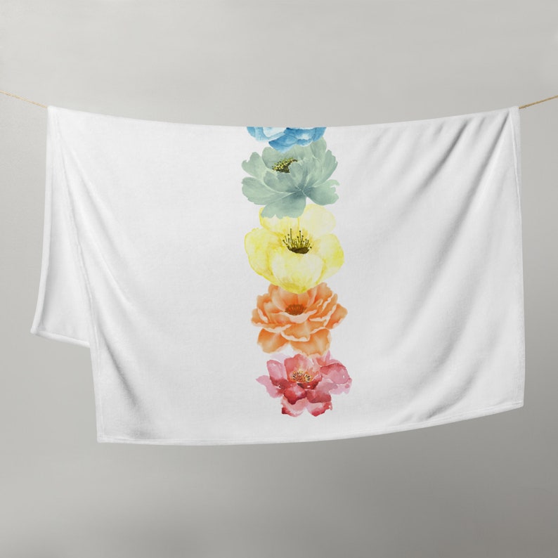 May include: A white throw blanket with a vertical row of five watercolor flowers in rainbow colors. The flowers are blue, green, yellow, orange, and pink.