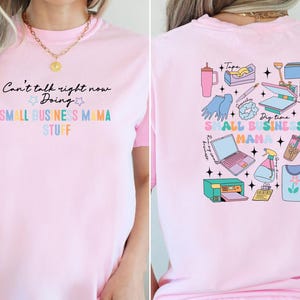 K&ouml;nnte beinhalten: Pinkes T-Shirt mit dem Text "Can't talk right now Doing SMALL BUSINESS MAMA STUFF" auf der Vorderseite und einer bunten Illustration von Kleinunternehmerbedarf auf der R&uuml;ckseite.