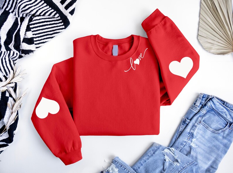 May include: Red sweatshirt with white hearts on the elbows and the word "love" with a heart on the chest.