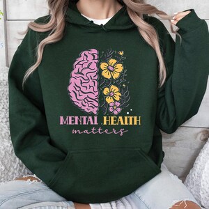 May include: A dark green hoodie with a pink and yellow brain with flowers graphic and the text "Mental Health matters".