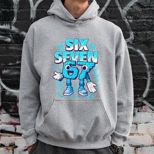 May include: A grey hoodie featuring the text "SIX SEVEN" in blue and white, with the numbers 6 and 7 designed as cartoon characters. The hoodie has a kangaroo pocket. The background is a brick wall with graffiti.