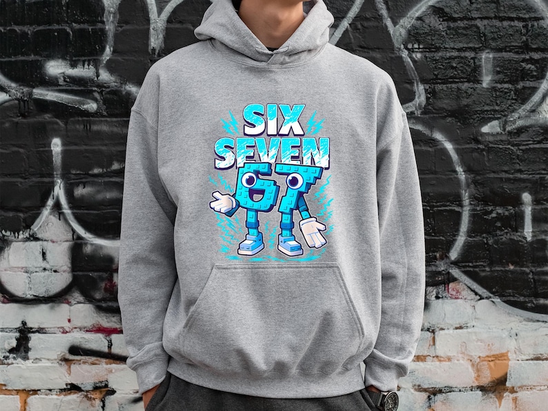 May include: A grey hoodie featuring the text "SIX SEVEN" in blue and white, with the numbers 6 and 7 designed as cartoon characters. The hoodie has a kangaroo pocket. The background is a brick wall with graffiti.