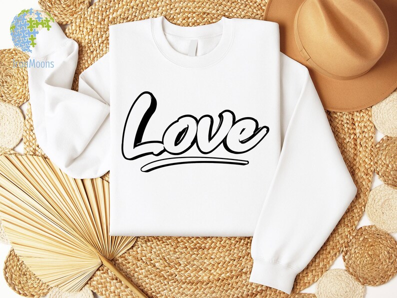 May include: White sweatshirt with the word "Love" printed in black, stylized lettering. The sweatshirt is laying on a woven straw surface.