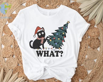 May include: White t-shirt featuring a black cat wearing a Santa hat and a scarf, pulling a Christmas tree. The text "WHAT?" is below the cat and tree. The tree is decorated with colorful lights and a star.