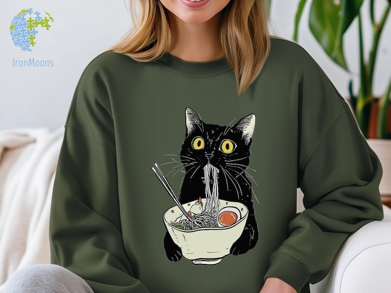 Peut inclure: Un chat noir aux yeux jaunes mange des nouilles ramen dans un bol blanc. Le chat porte un sweat-shirt vert avec un motif de chat mangeant des nouilles ramen.