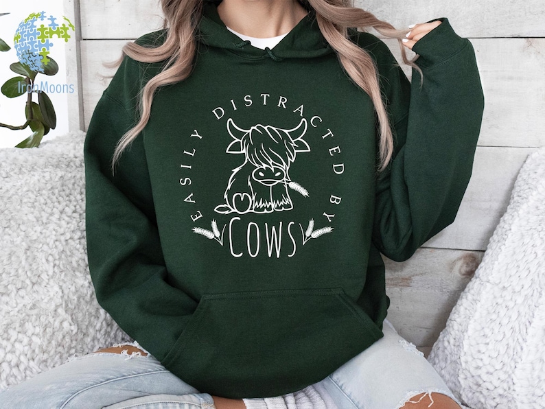 May include: A dark green hoodie with a white graphic that says "Easily Distracted By Cows" and features a cartoon cow with a heart on its chest.