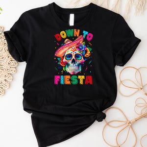 May include: Black t-shirt with a colorful sugar skull wearing a sombrero and the text "Down to Fiesta".
