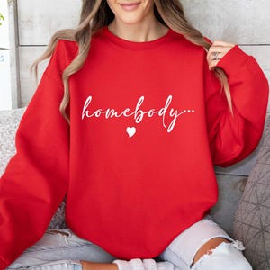 May include: Red sweatshirt with the text "homebody..." in white lettering and a small white heart.