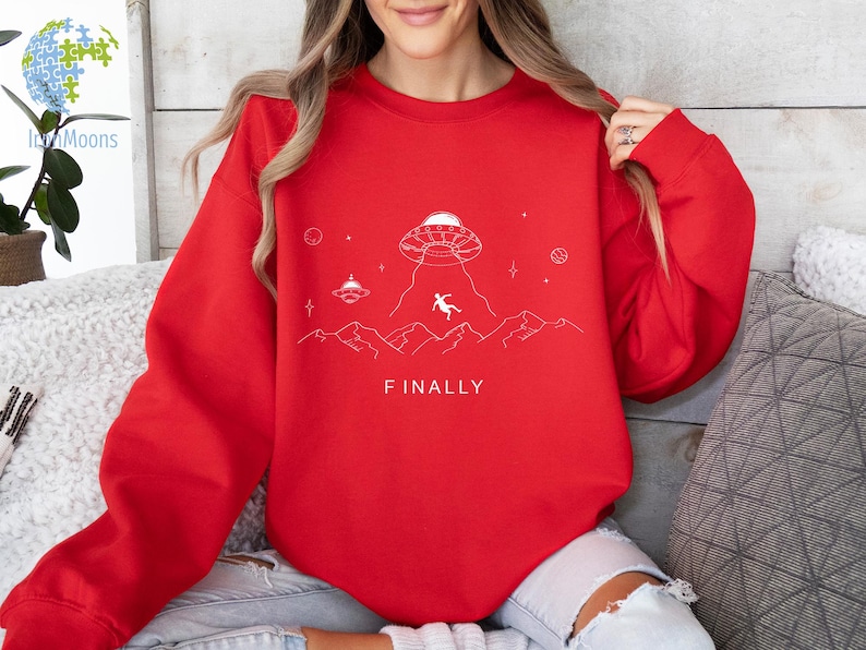 K&ouml;nnte beinhalten: Roter Pullover mit einem wei&szlig;en Aufdruck eines UFOs, einer Person, die aus dem UFO f&auml;llt, und dem Text "FINALLY".