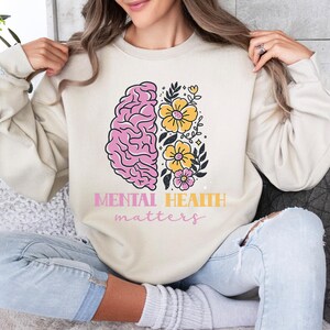 May include: A cream-colored sweatshirt with a pink and white brain graphic and yellow flowers. The text "Mental Health matters" is printed below the graphic.